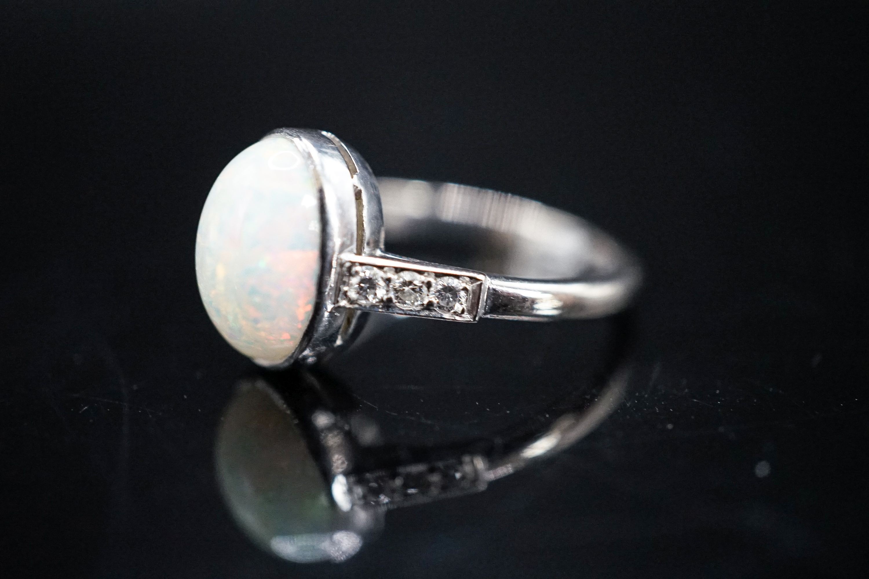 A white metal and white opal set oval ring, with diamond set shoulders, size M, gross weight 3.4 grams.